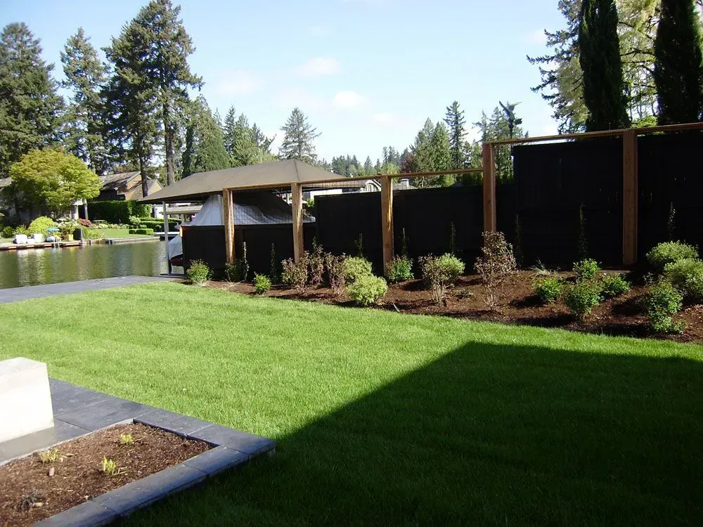Landscaped garden with green lawn, shrubs, trees, and a covered patio under a clear sky
