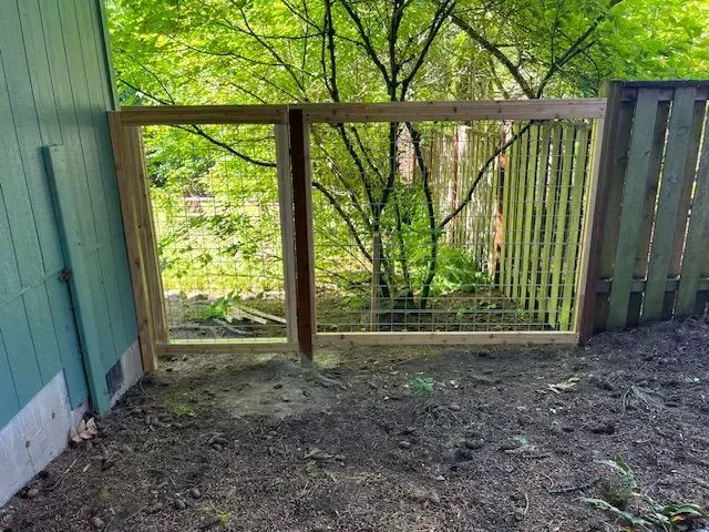 Wooden porch railing overlooking a wooded backyard, with a green-painted house wall on the left.