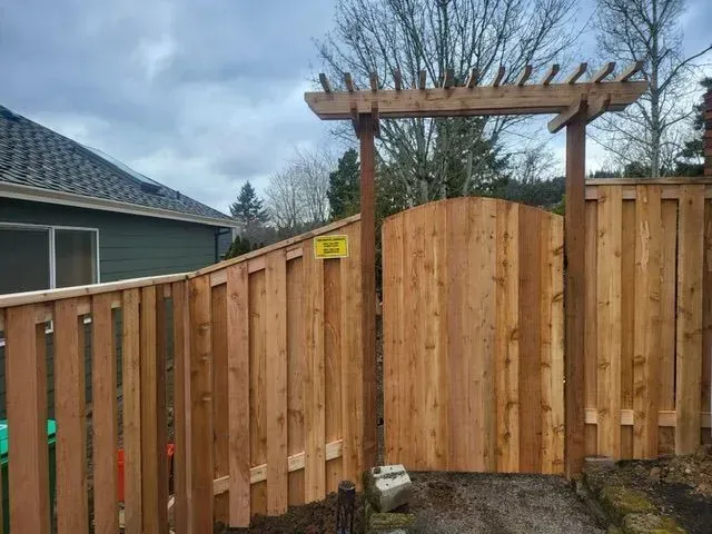 Wooden backyard fence with a curved gate and pergola against a cloudy sky