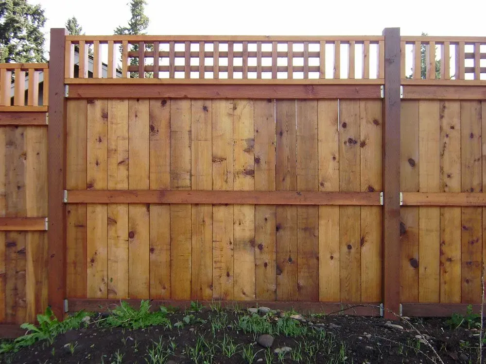 Wooden privacy fence with lattice top in a yard, bordered by greenery.