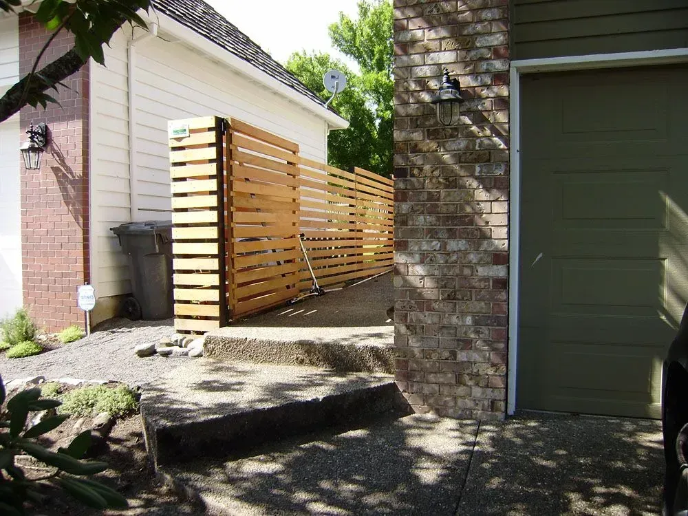 Wooden slat fence beside a house, blocking a side yard walkway next to a garage.