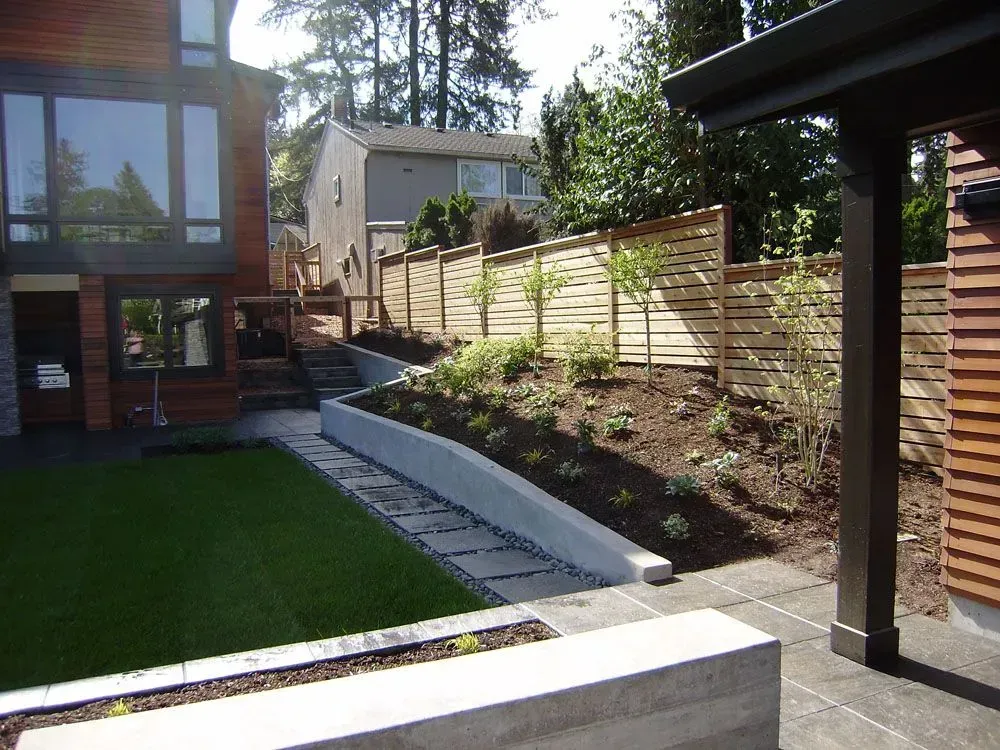 Modern backyard with patio, lawn, retaining wall, and wooden fence in sunlight