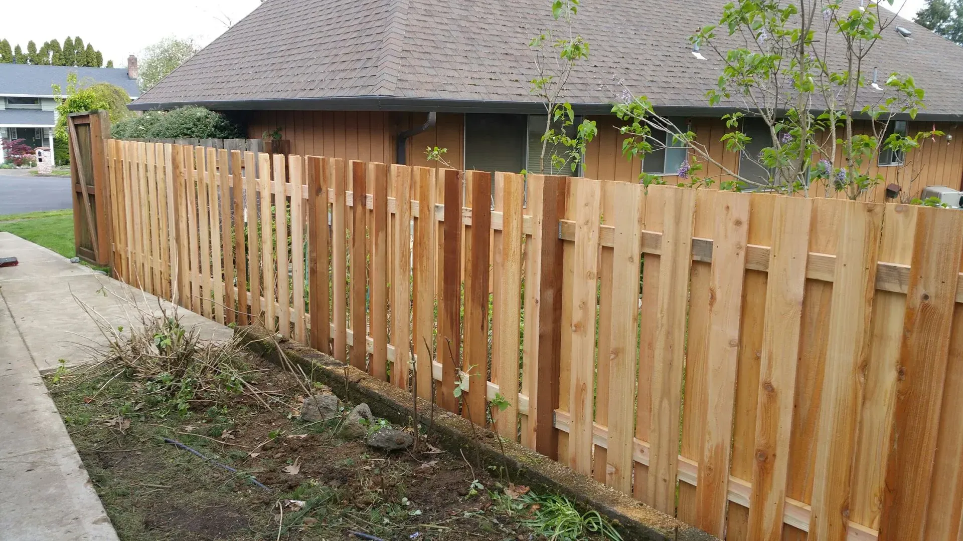 Wooden privacy fence along a driveway beside a house and sidewalk