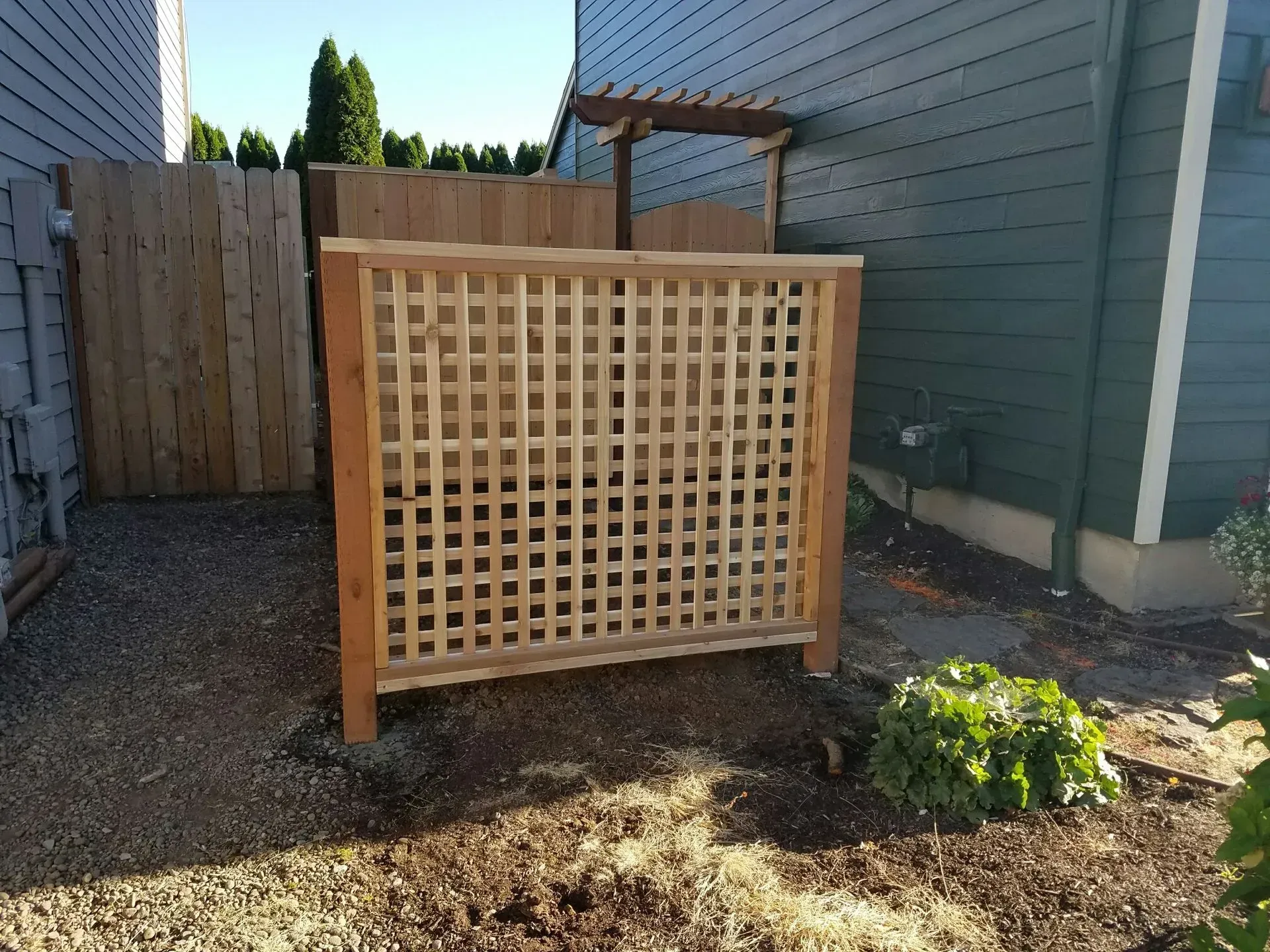 Wooden lattice garden screen beside a house, with a small plant bed in front.