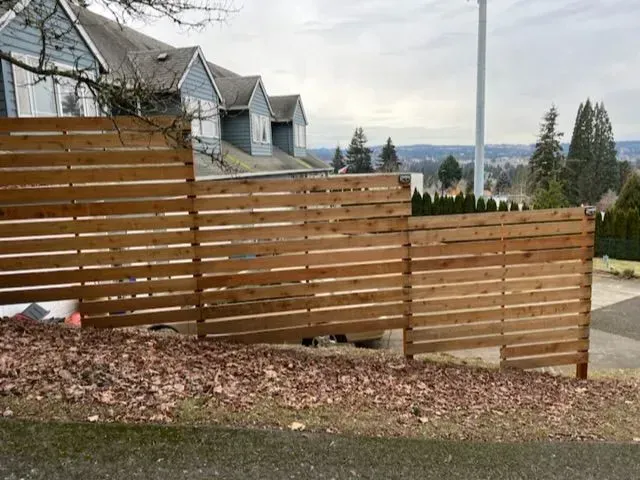 Wooden privacy fence on a sloped yard with houses and a distant city view behind it