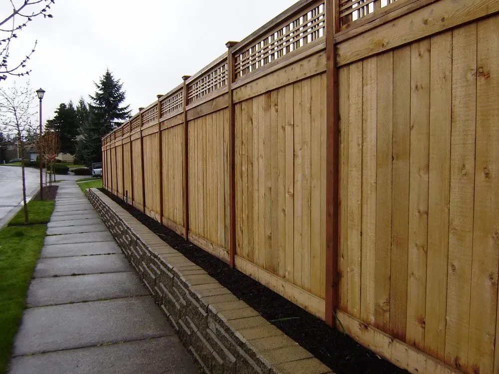 Sidewalk beside a long wooden privacy fence on a cloudy street.