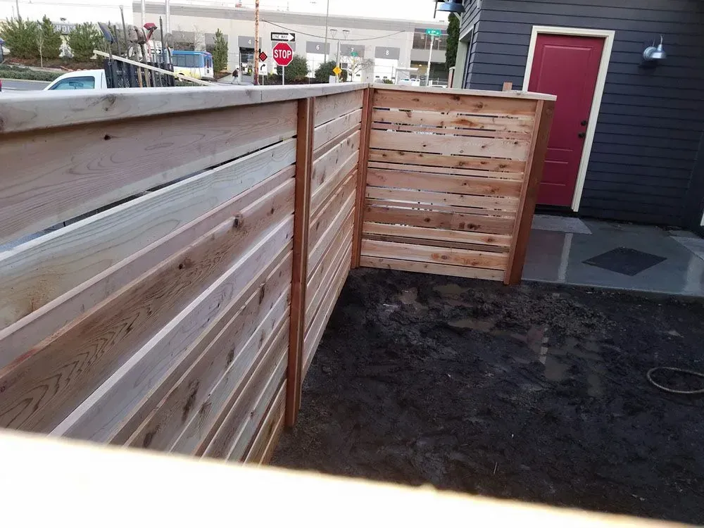 Wooden privacy fence beside a building with a red door and gravel ground.