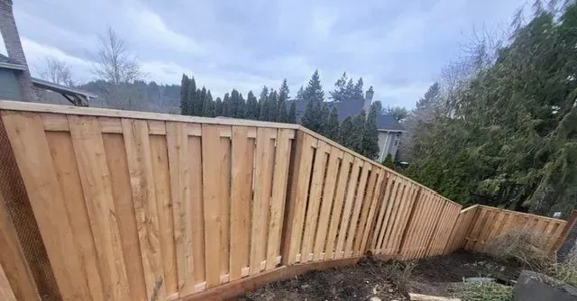 Wooden fence panels along a sloped yard with trees and mountains in the background