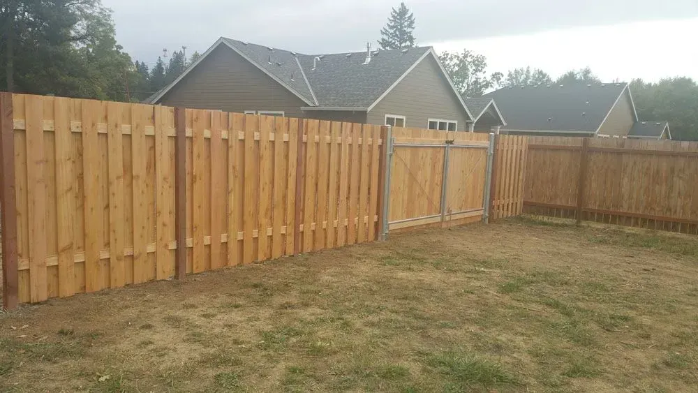 Wooden privacy fence around a grassy backyard with houses and trees in the background