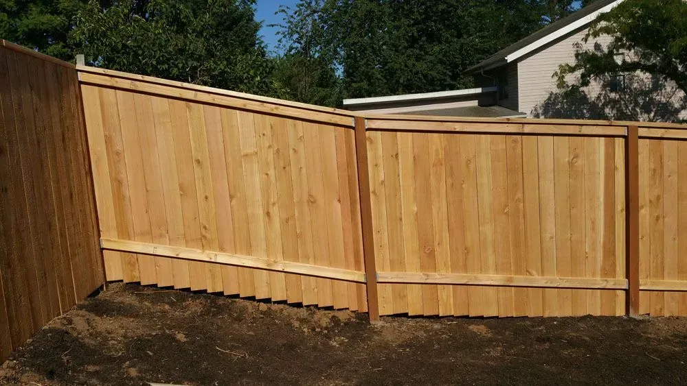 Wooden privacy fence in a backyard, with tan panels and horizontal support rails under a sunny sky.