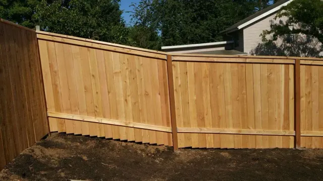 New wooden privacy fence with tan panels and darker trim around a backyard corner