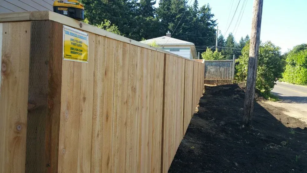 New wooden fence along a roadside with dirt and trees in the background