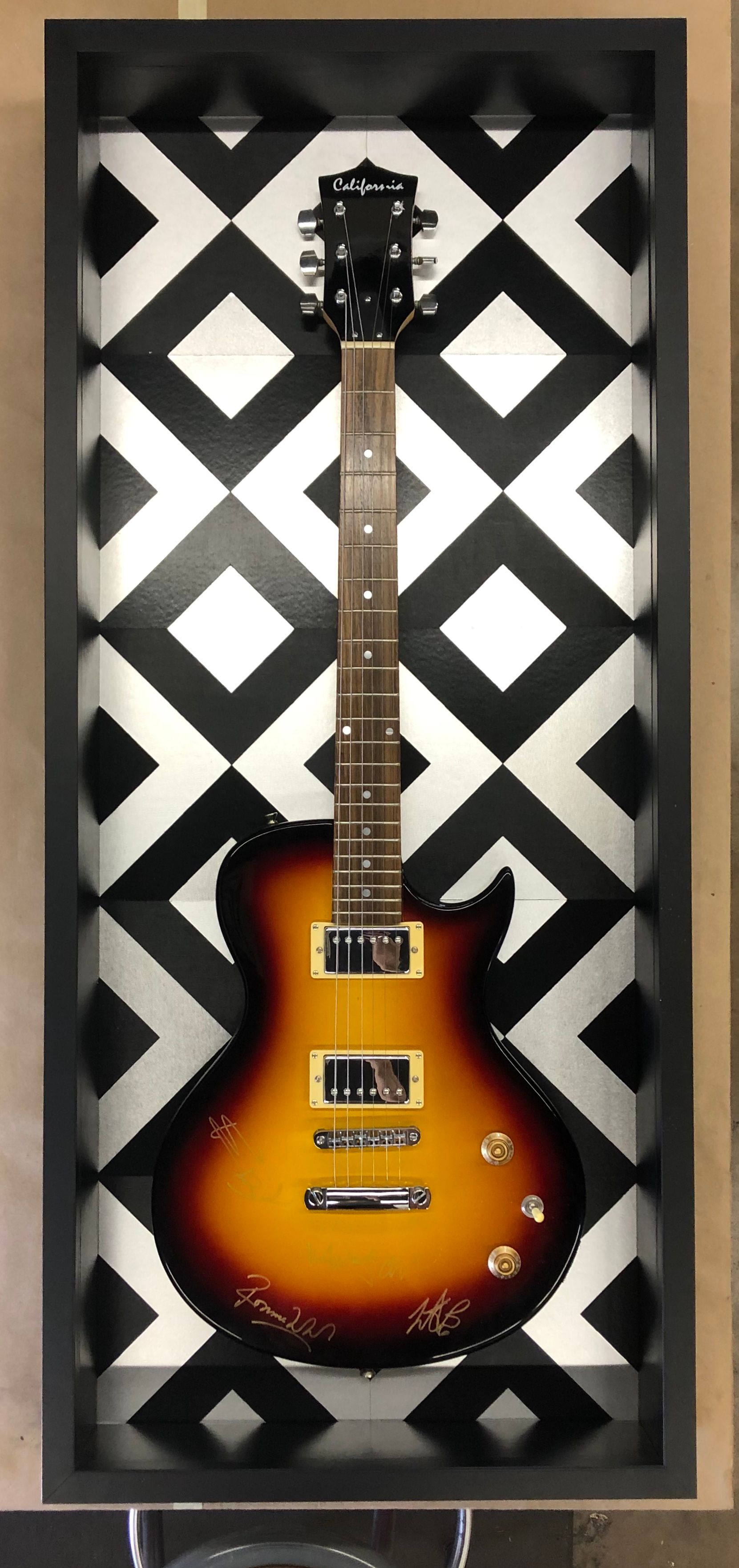 A guitar is displayed in a black and white checkered frame