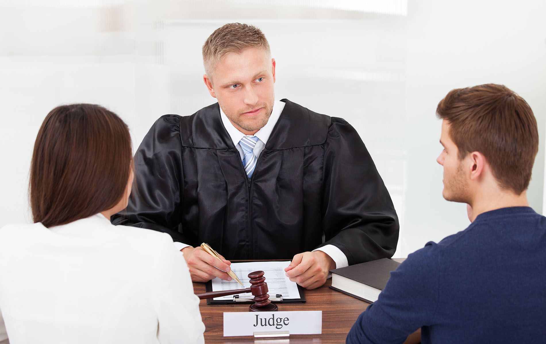 Judge in black robe speaking to a couple, likely in a courtroom.