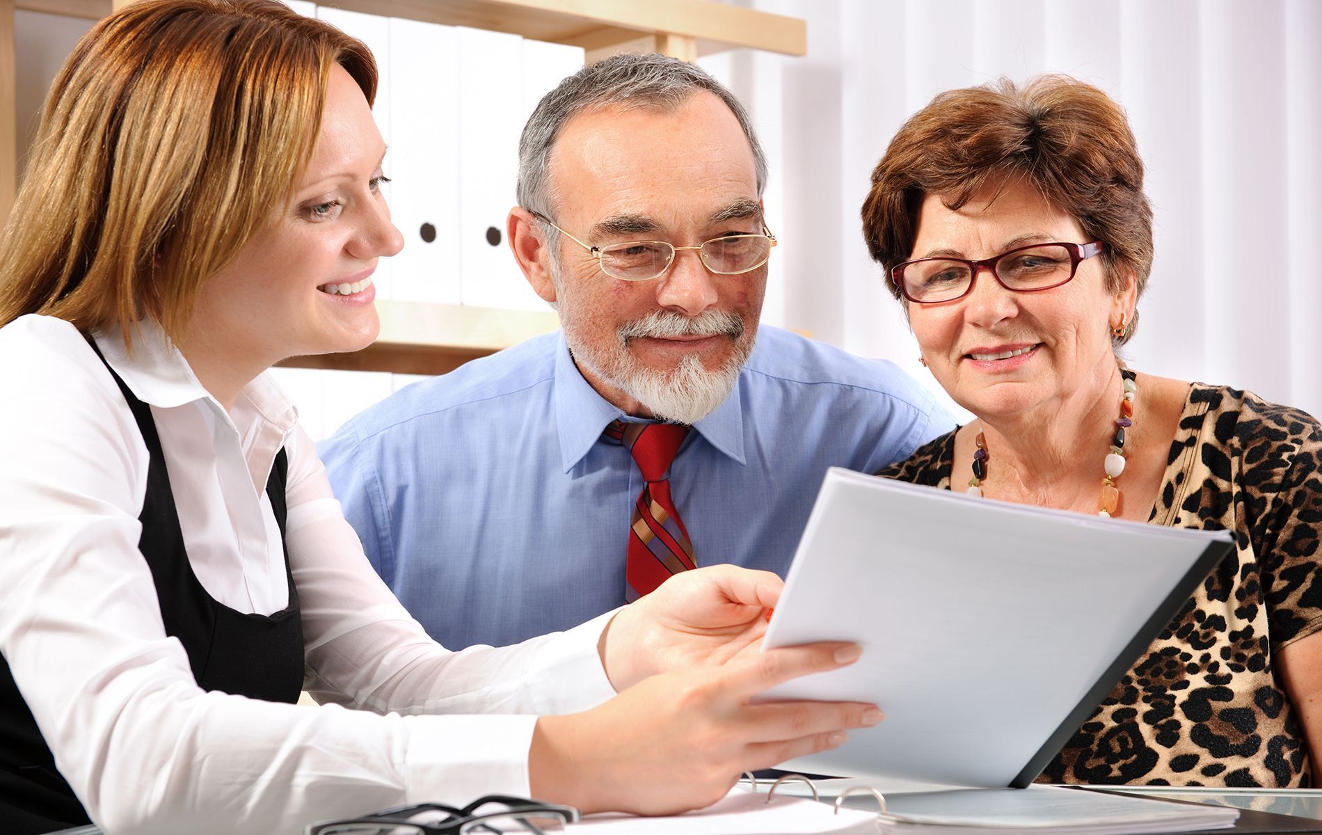 A financial advisor reviews documents with a smiling elderly couple in an office setting.