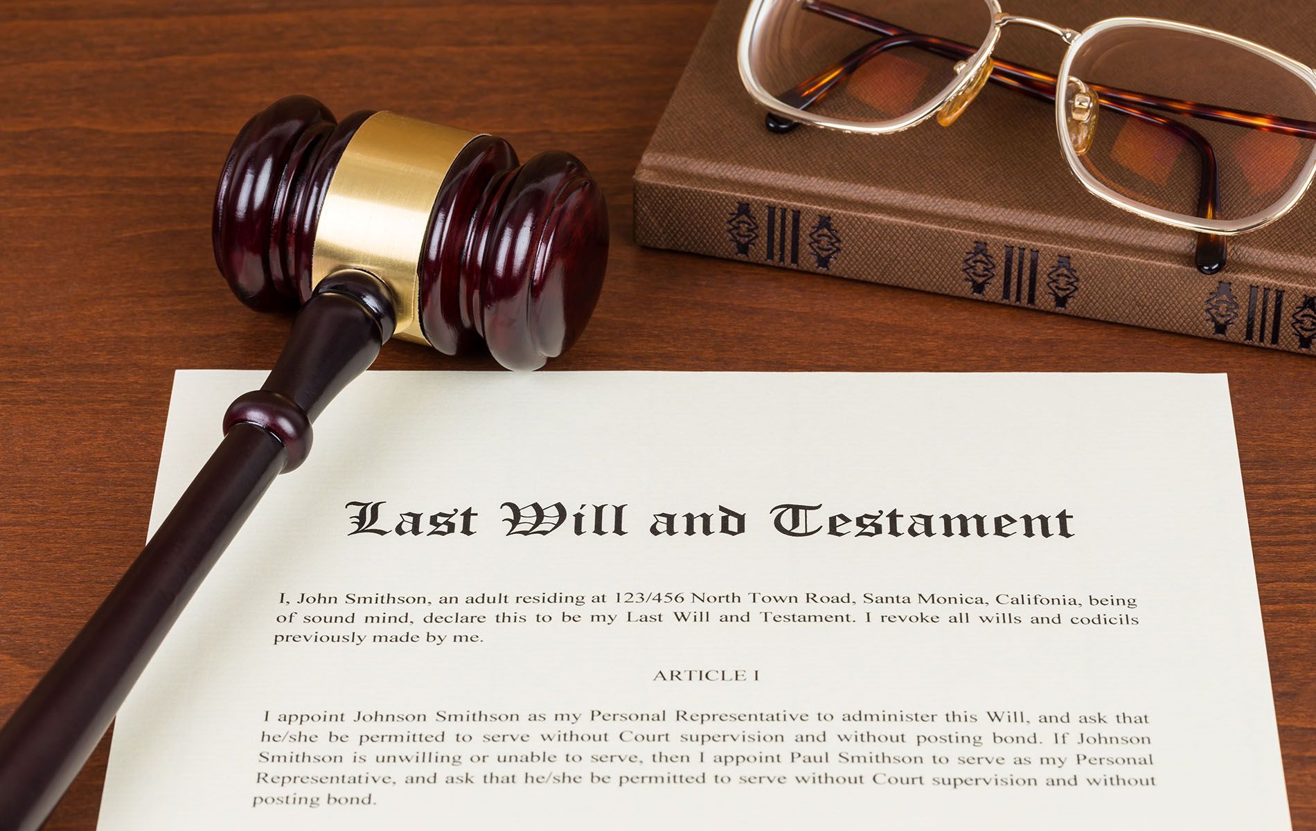 Gavel on Last Will and Testament document next to a book and glasses on a wooden surface.