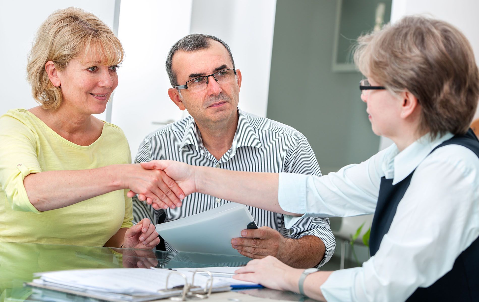 A man and woman are shaking hands with a woman while sitting at a table.