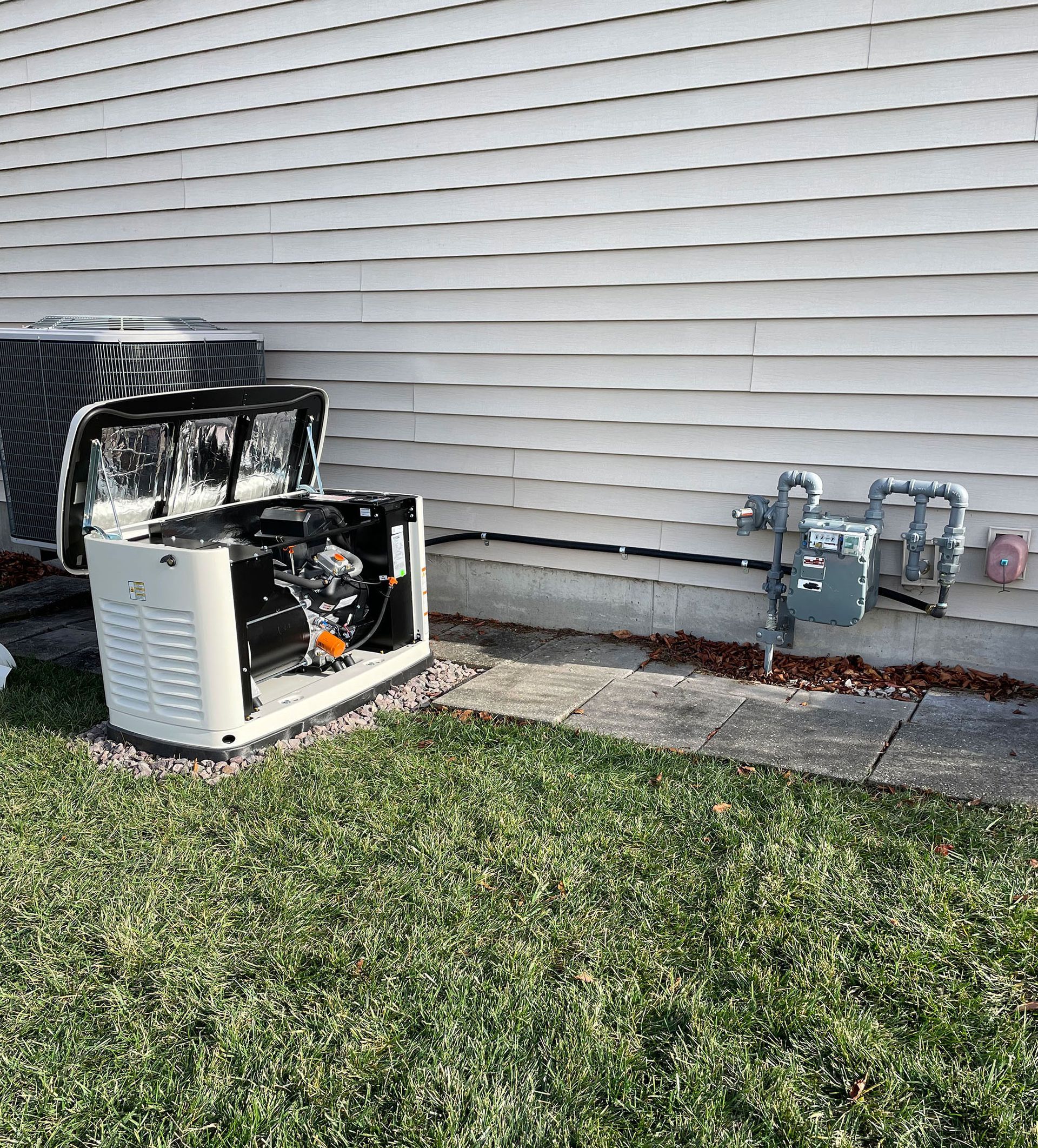 A generator is sitting in the grass next to a house.