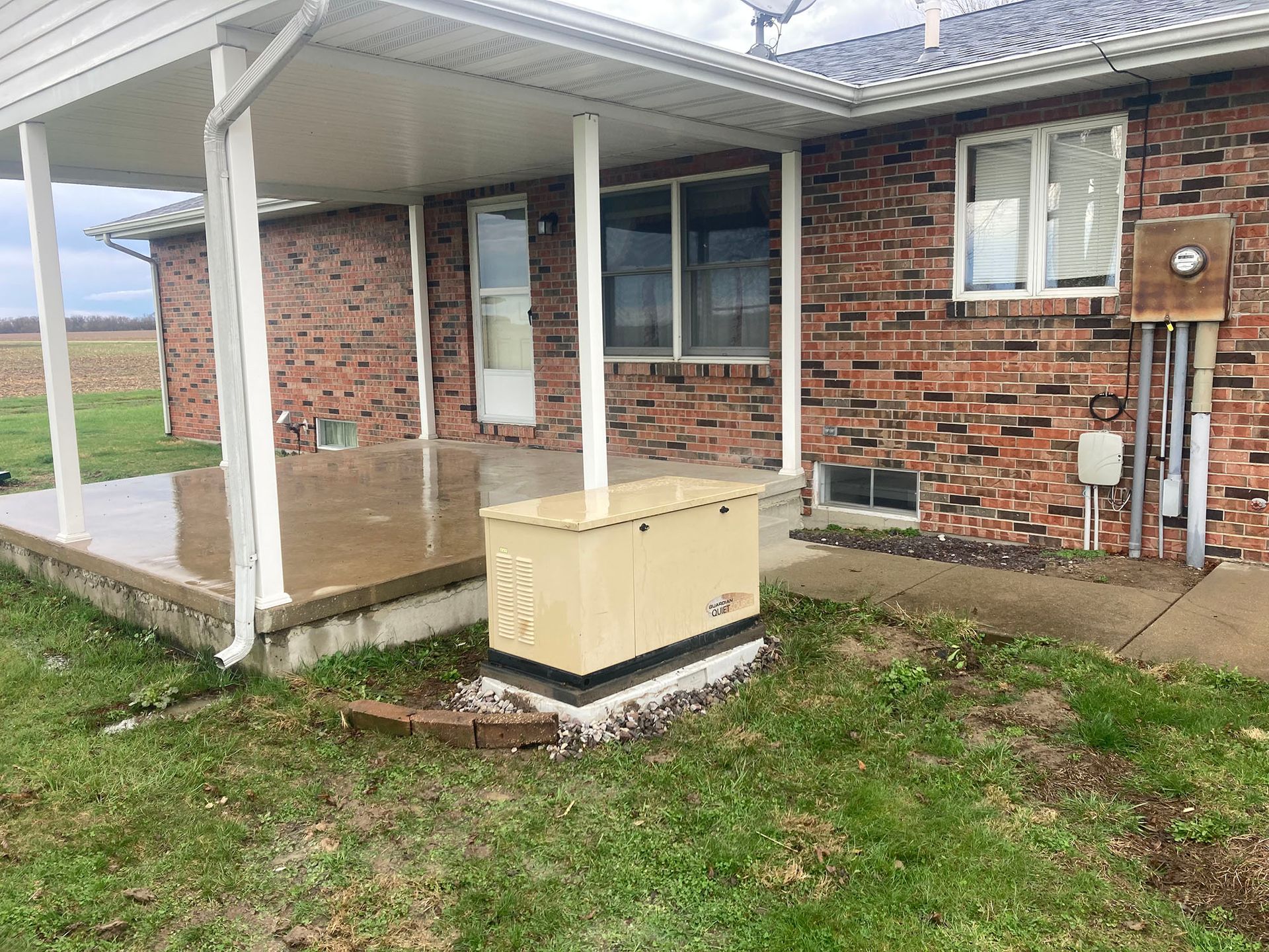 A brick house with a porch and a generator in front of it.