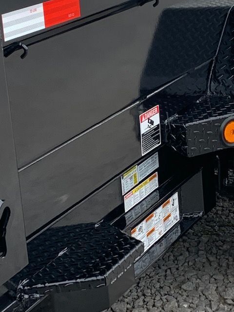 Black trailer with warning labels and diamond plate steps.