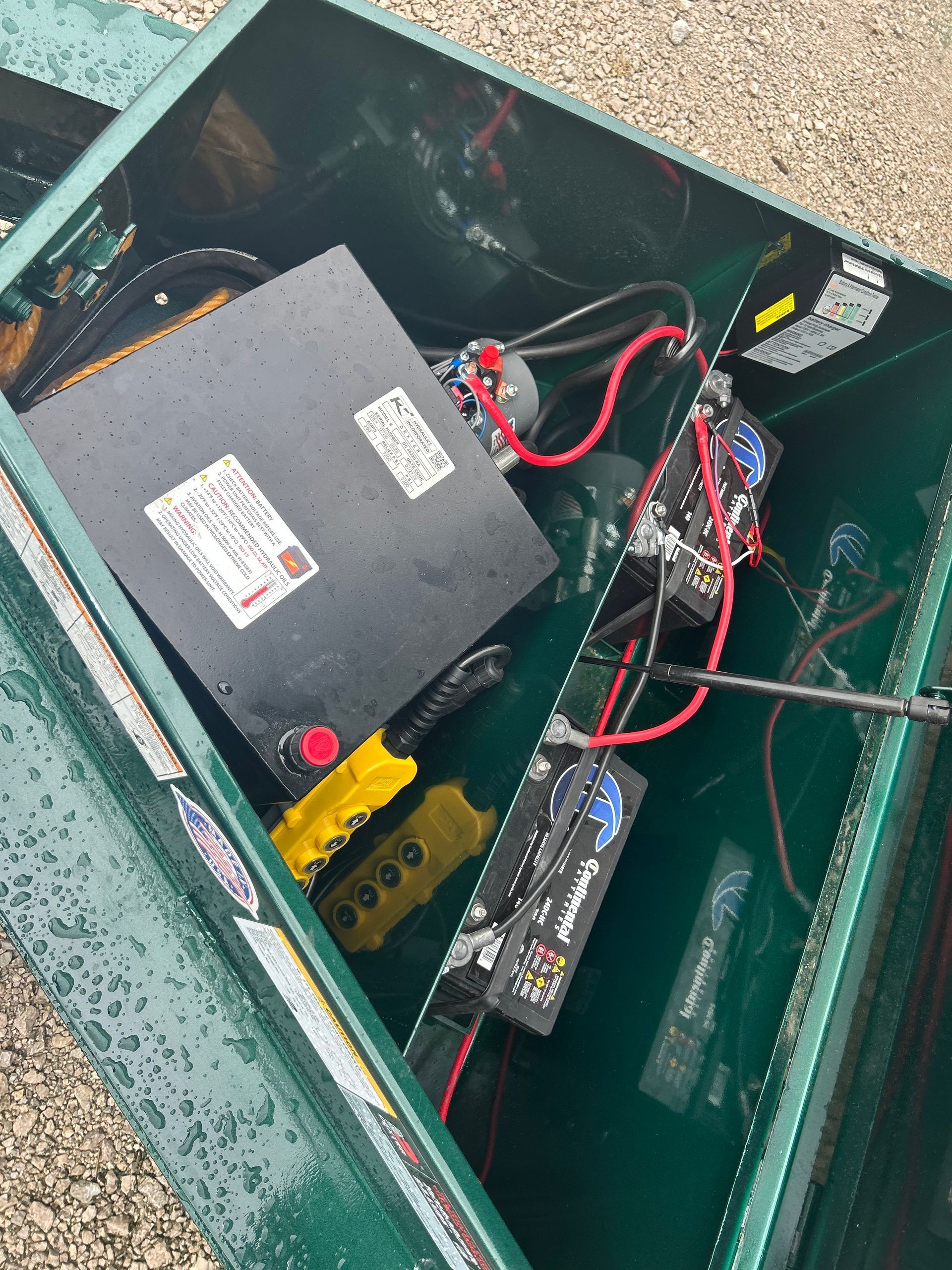 Open electrical box with battery, wires, and control components inside a green enclosure.