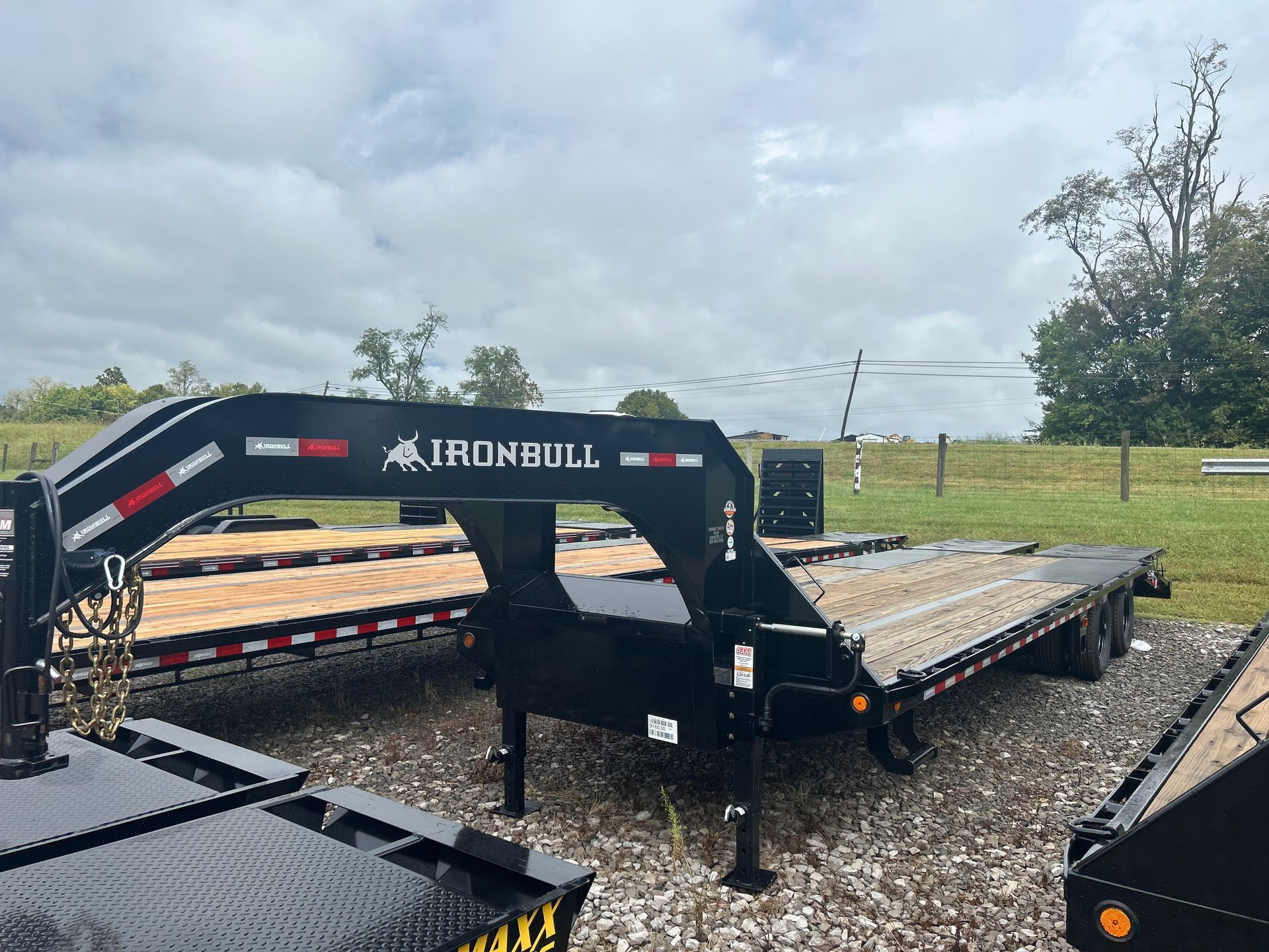 Black Ironbull equipment trailer with folded ramp on gravel lot under cloudy sky