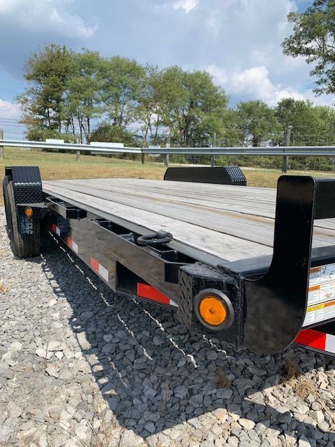 Black flatbed trailer with wooden deck on gravel.