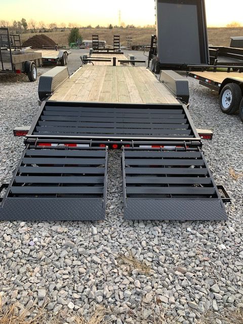 Black and wood-floored trailer with fold-down ramps on a gravel lot, ready for loading.