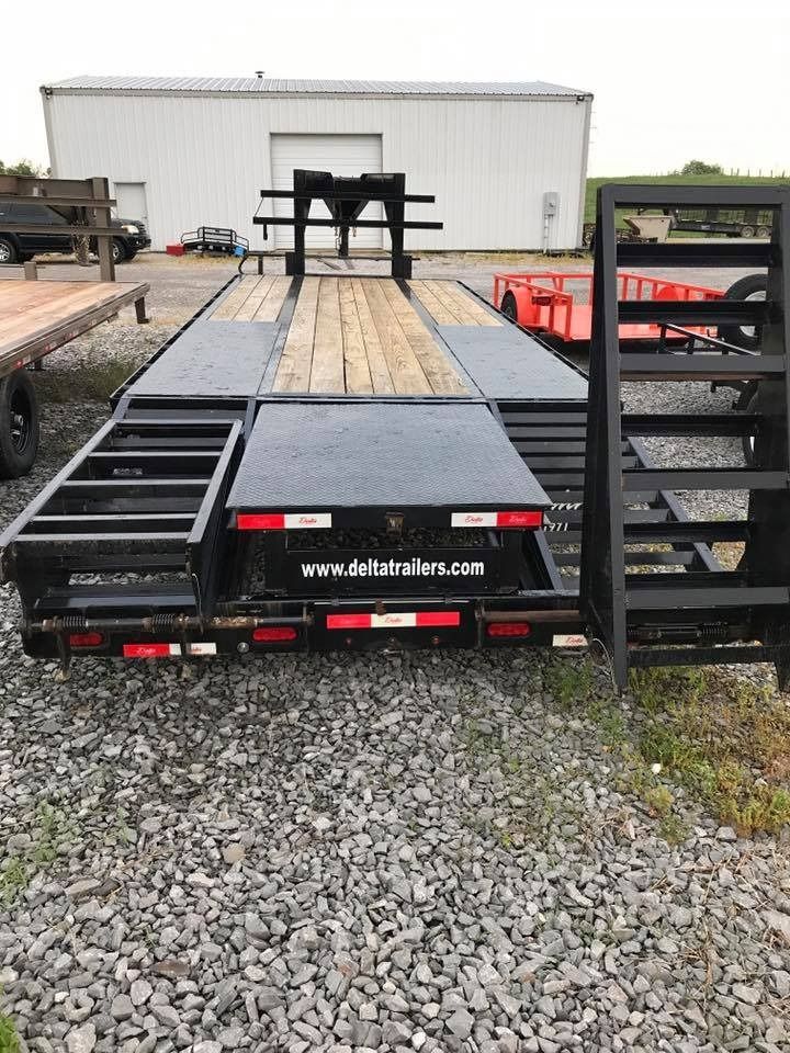 Black Delta trailer with wooden deck, rear ramps, and gray gravel.