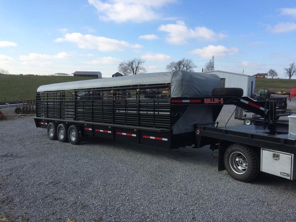 Livestock trailer hitched to a flatbed truck on gravel, under a cloudy sky.