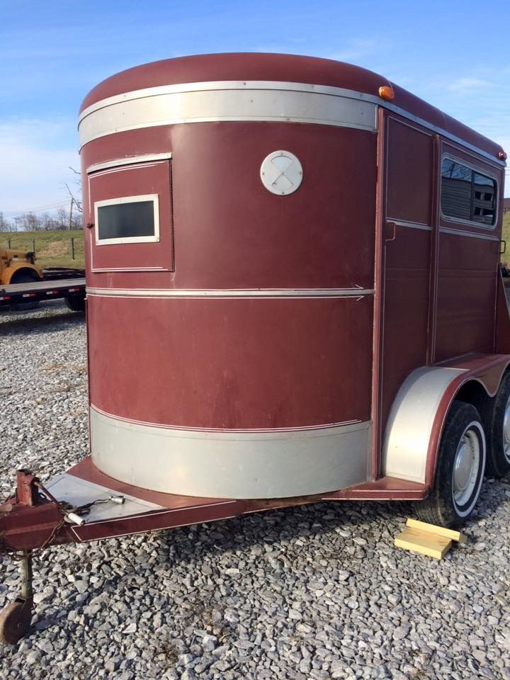 Maroon and silver horse trailer with windows parked on gravel.