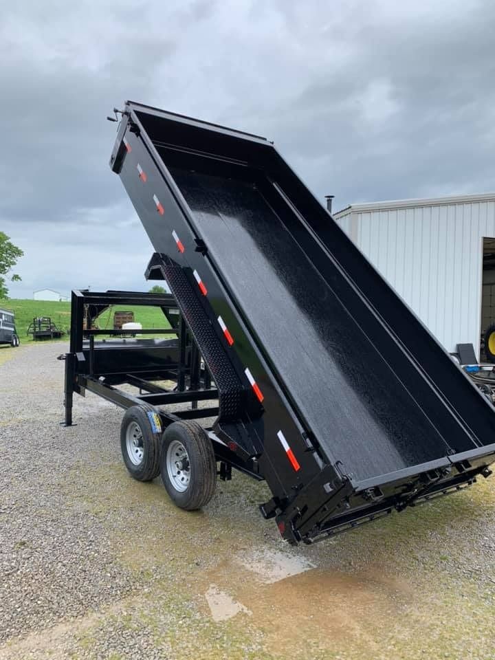 Black dump trailer with the bed raised, parked on gravel.