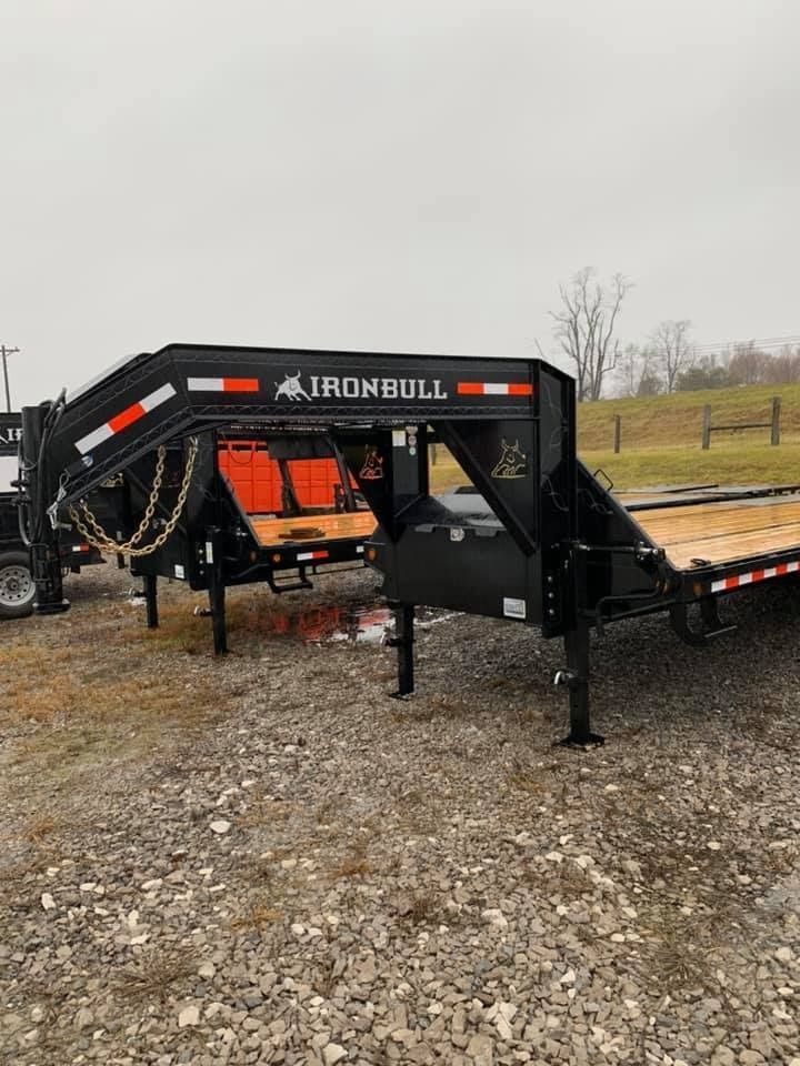 Black Iron Bull gooseneck trailer on a gravel lot; orange and white accents, cloudy day.