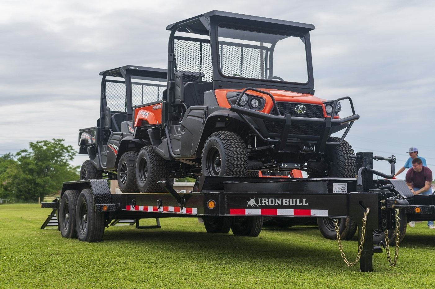 Two orange utility vehicles with protective cages on a trailer in a grassy field.
