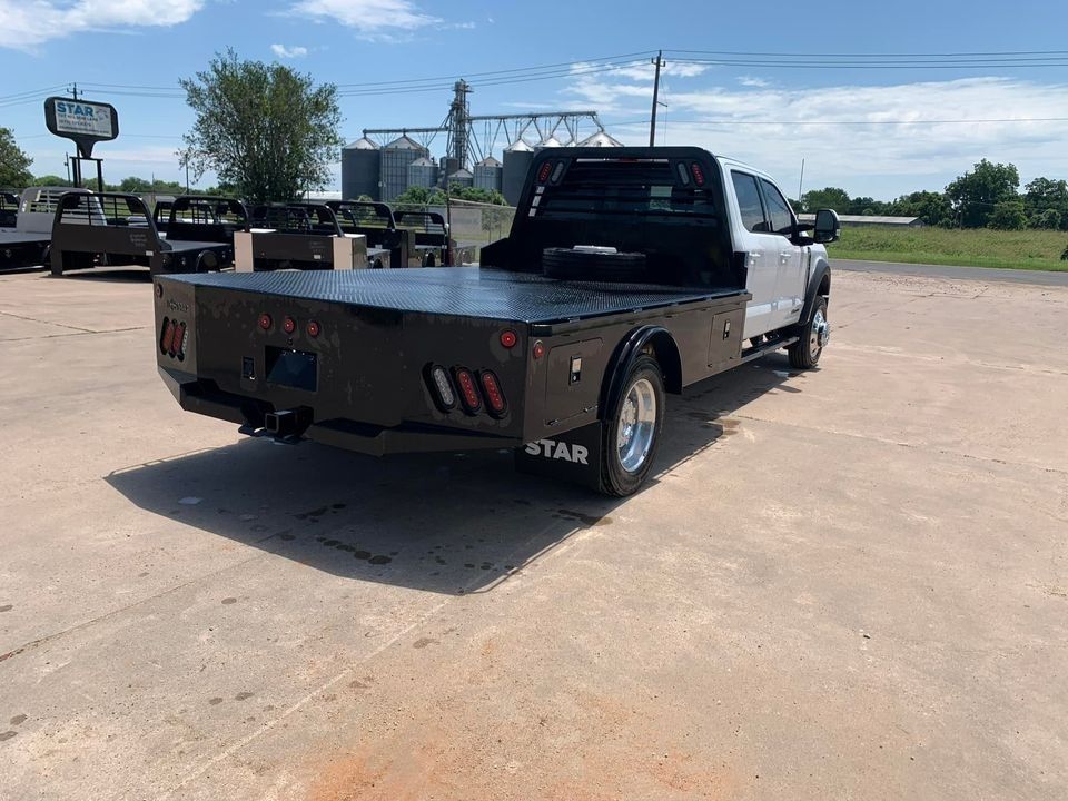 White flatbed truck, black bed, sunny outdoor setting.