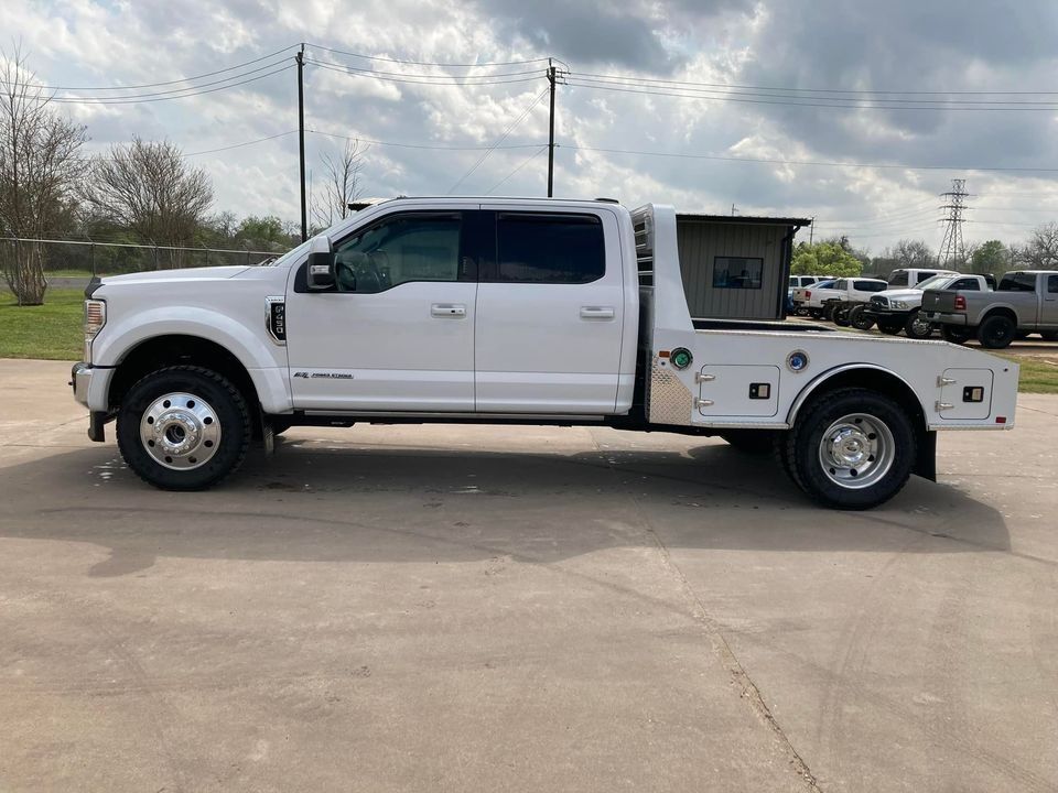 White Ford truck with a flatbed in a parking lot.