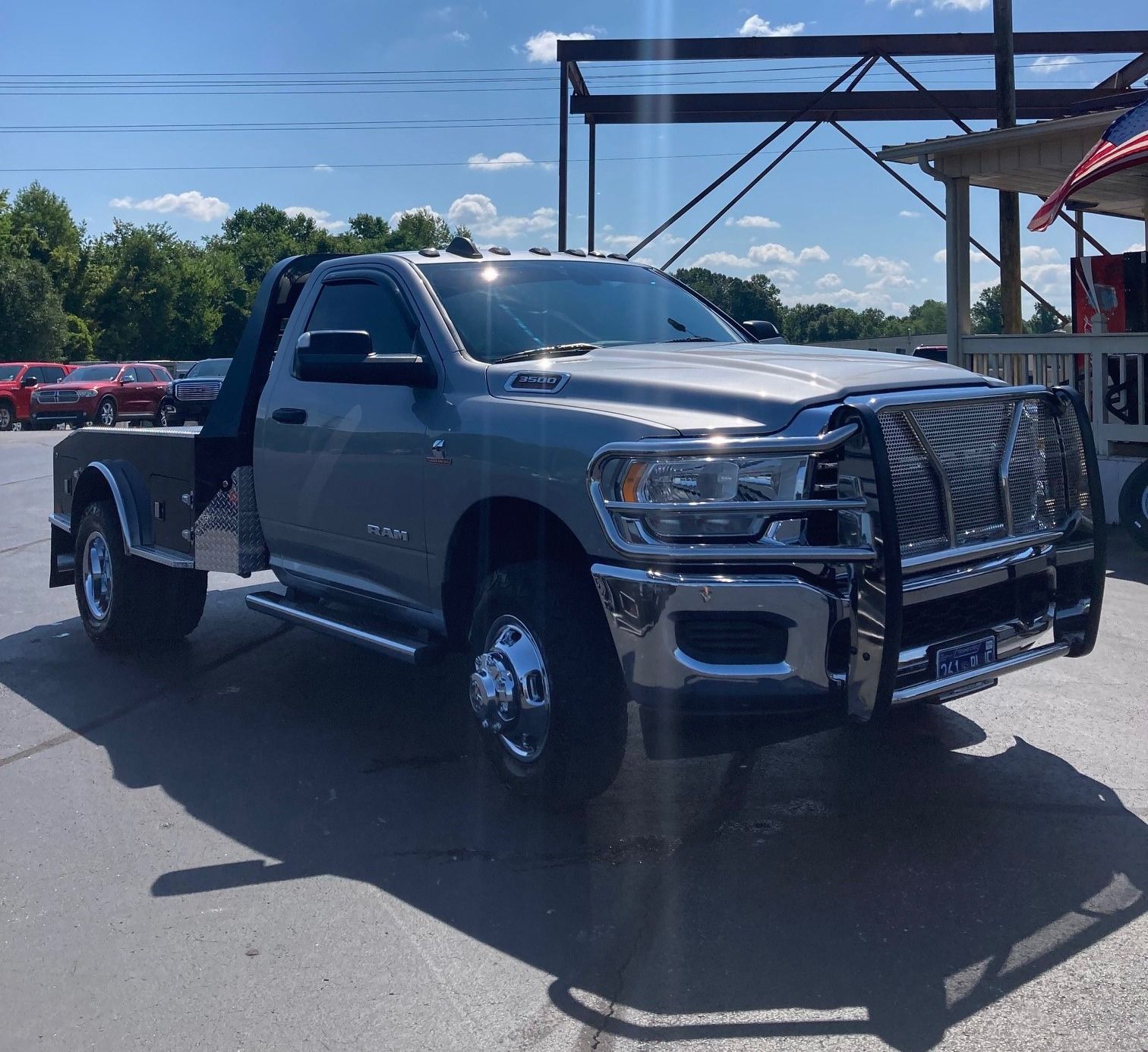 Gray Ram pickup truck with flatbed and brush guard parked outside on a sunny day.