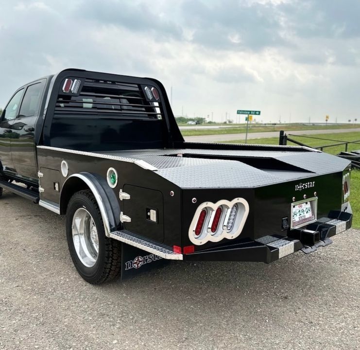 Black flatbed truck with diamond-plate detailing and LED taillights parked on a gravel roadside.