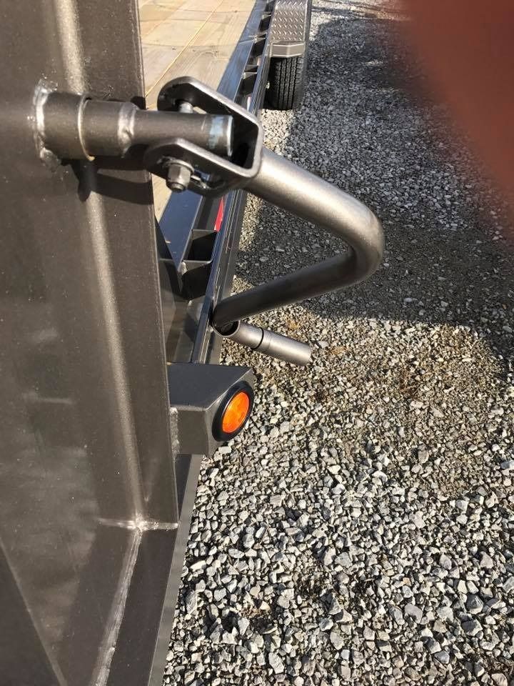 Silver trailer latch with a handle, next to a warning light on a gravel surface.