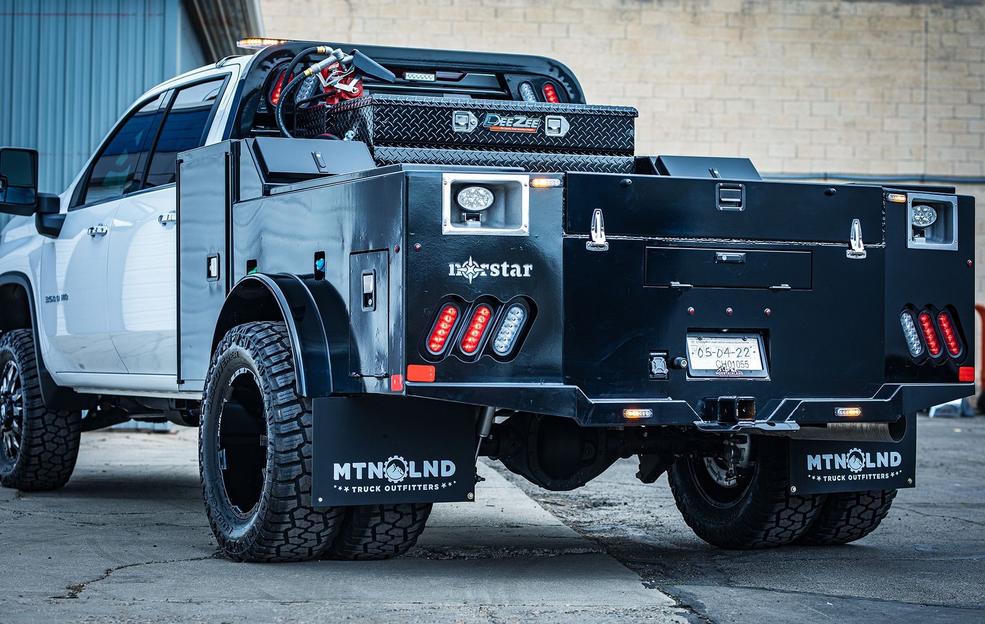 White pickup truck with a black utility bed, featuring storage boxes and lights.