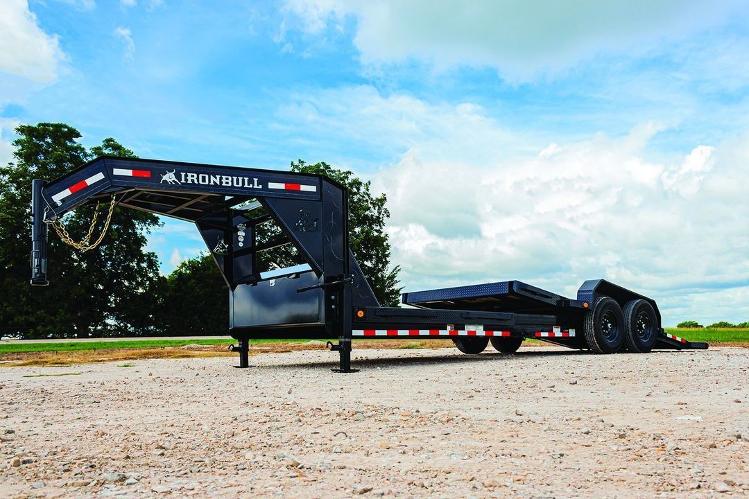 Black gooseneck trailer on a gravel surface under a partly cloudy sky.