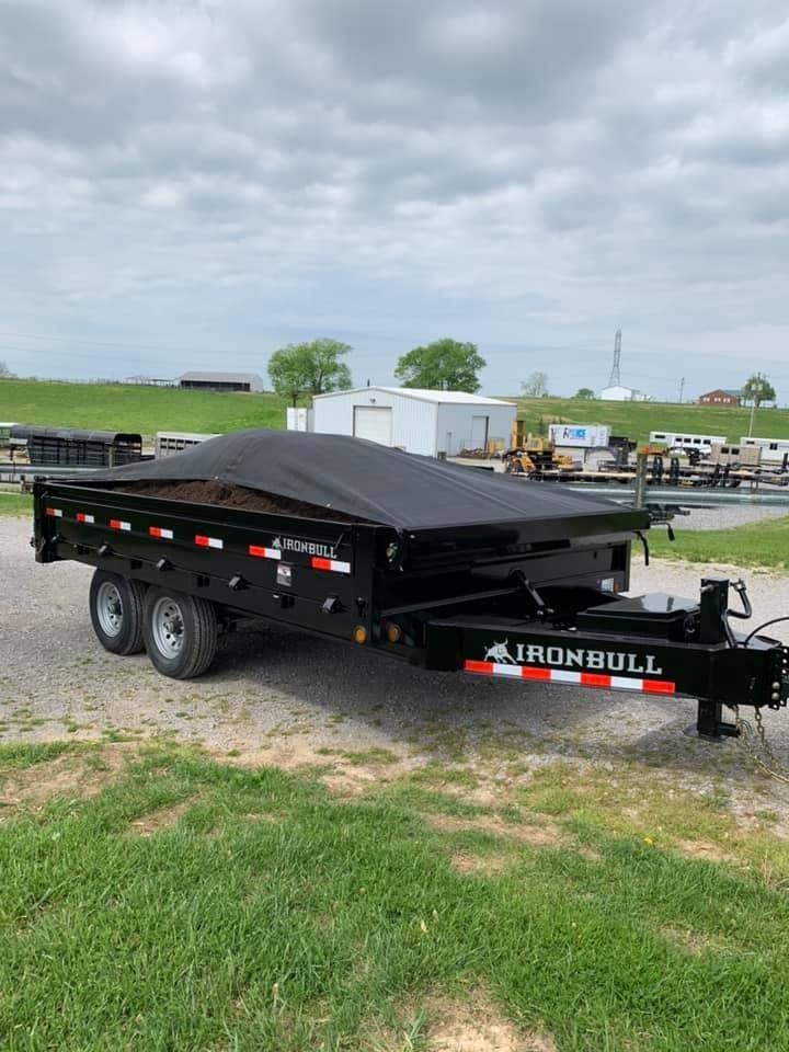 Black Ironbull dump trailer with tarp cover, parked on grass.