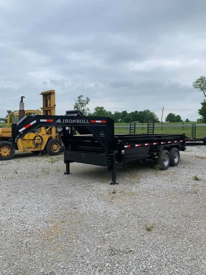 Black Iron Bull gooseneck trailer on gravel, yellow loader in background.