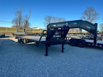 Black gooseneck trailer parked on gravel, clear sky in the background.