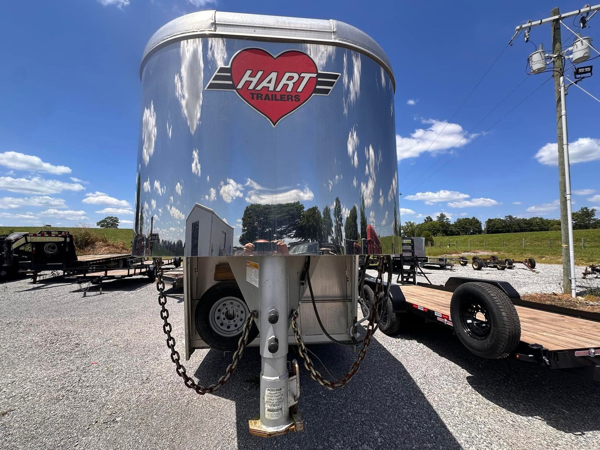 Shiny silver HART trailer with red logo on a gravel lot under a blue sky