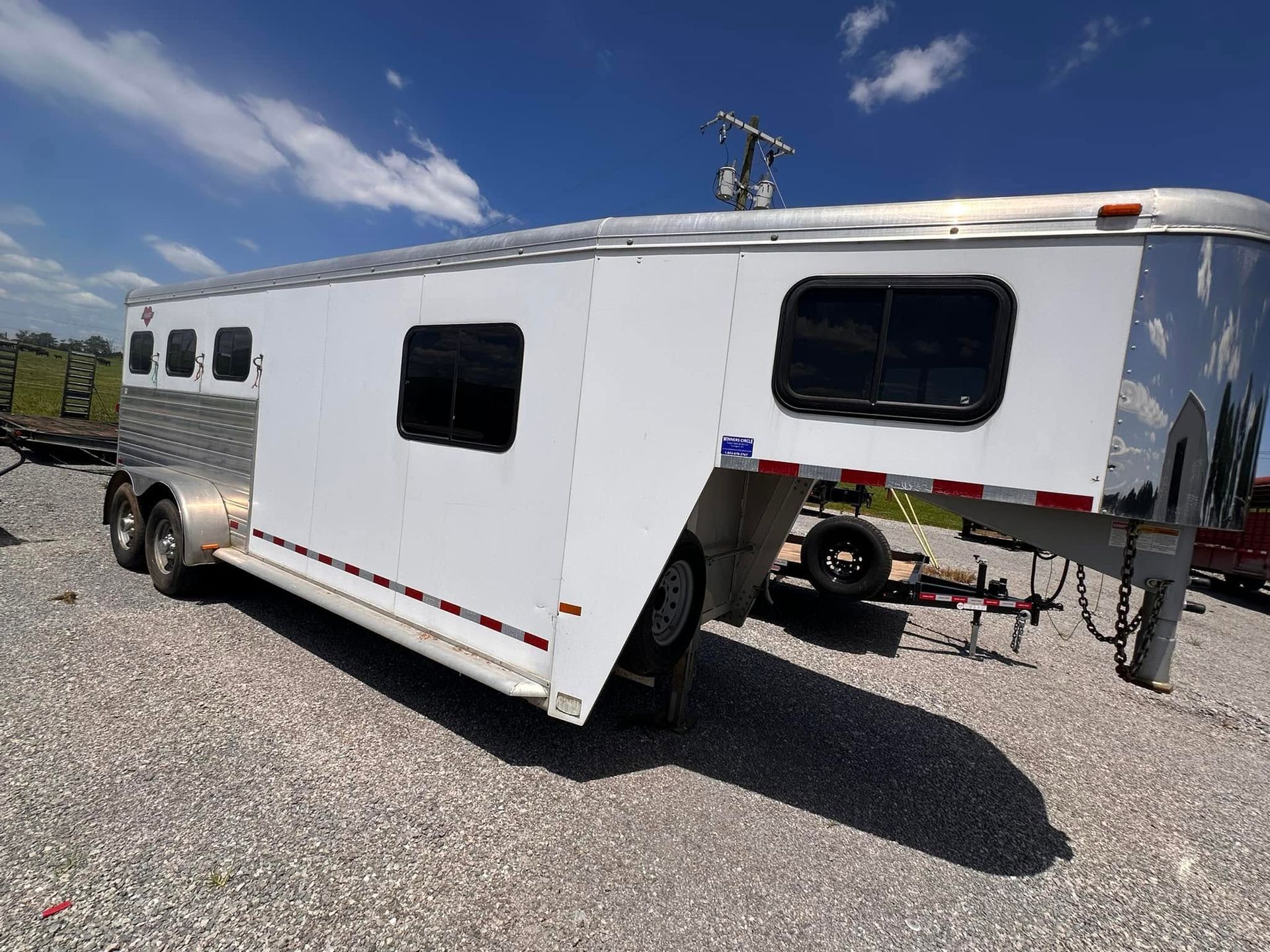 White tandem-axle trailer with gooseneck hitch parked on gravel under a blue sky