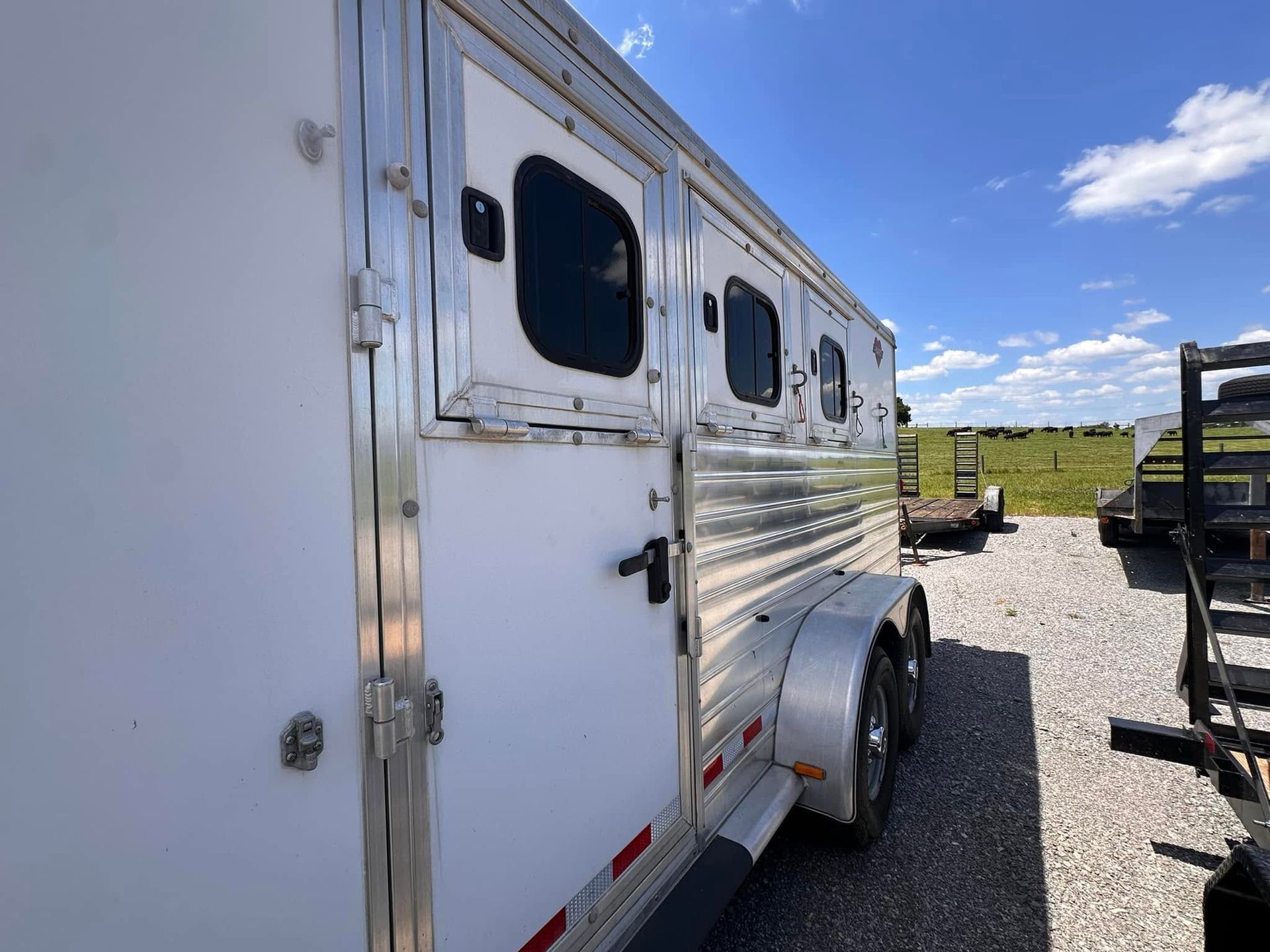 White horse trailer parked on gravel under a blue sky, with another trailer in the background.