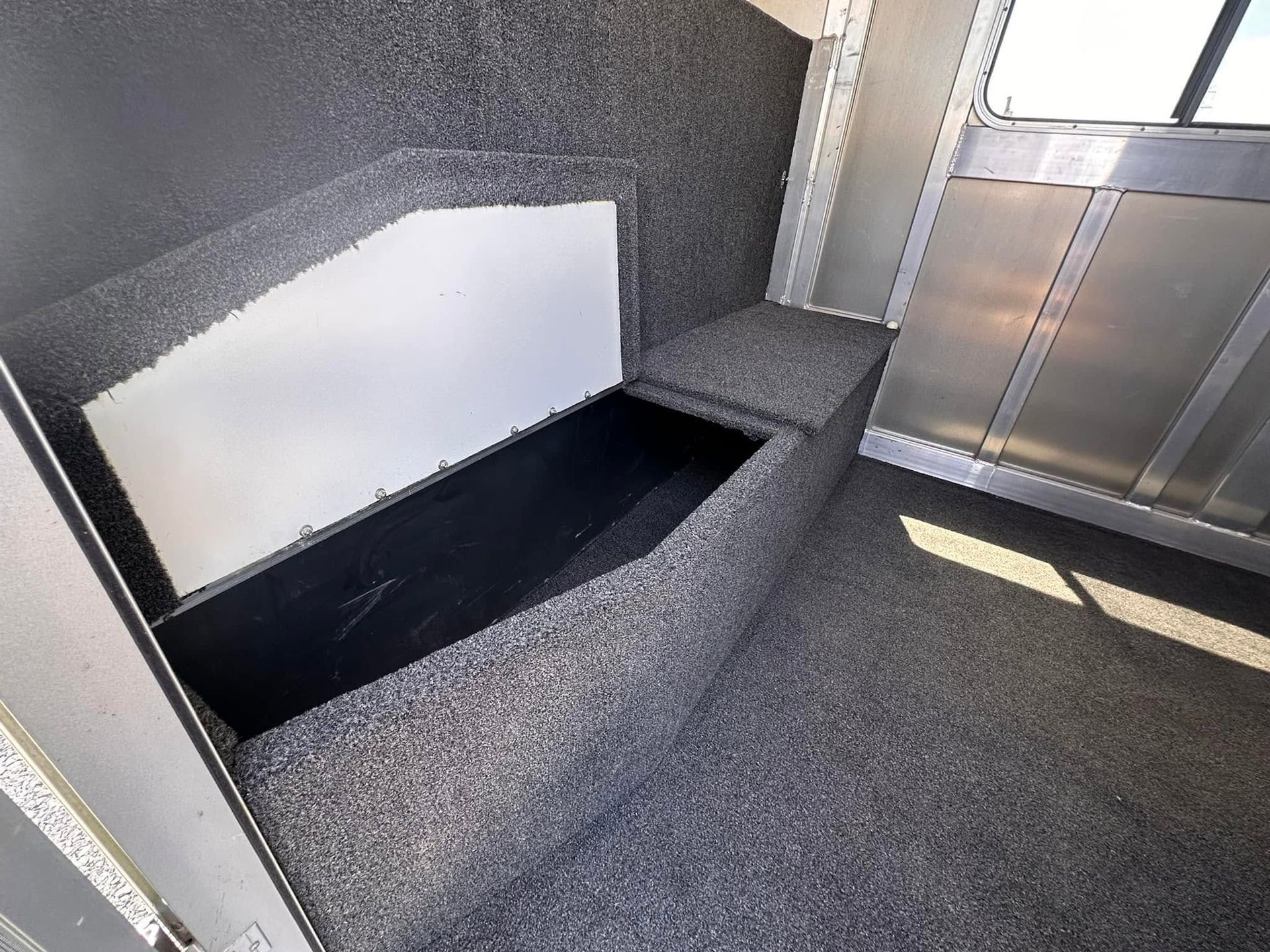Gray carpeted interior nook with a black rectangular opening, white panel, and metal door or panel nearby