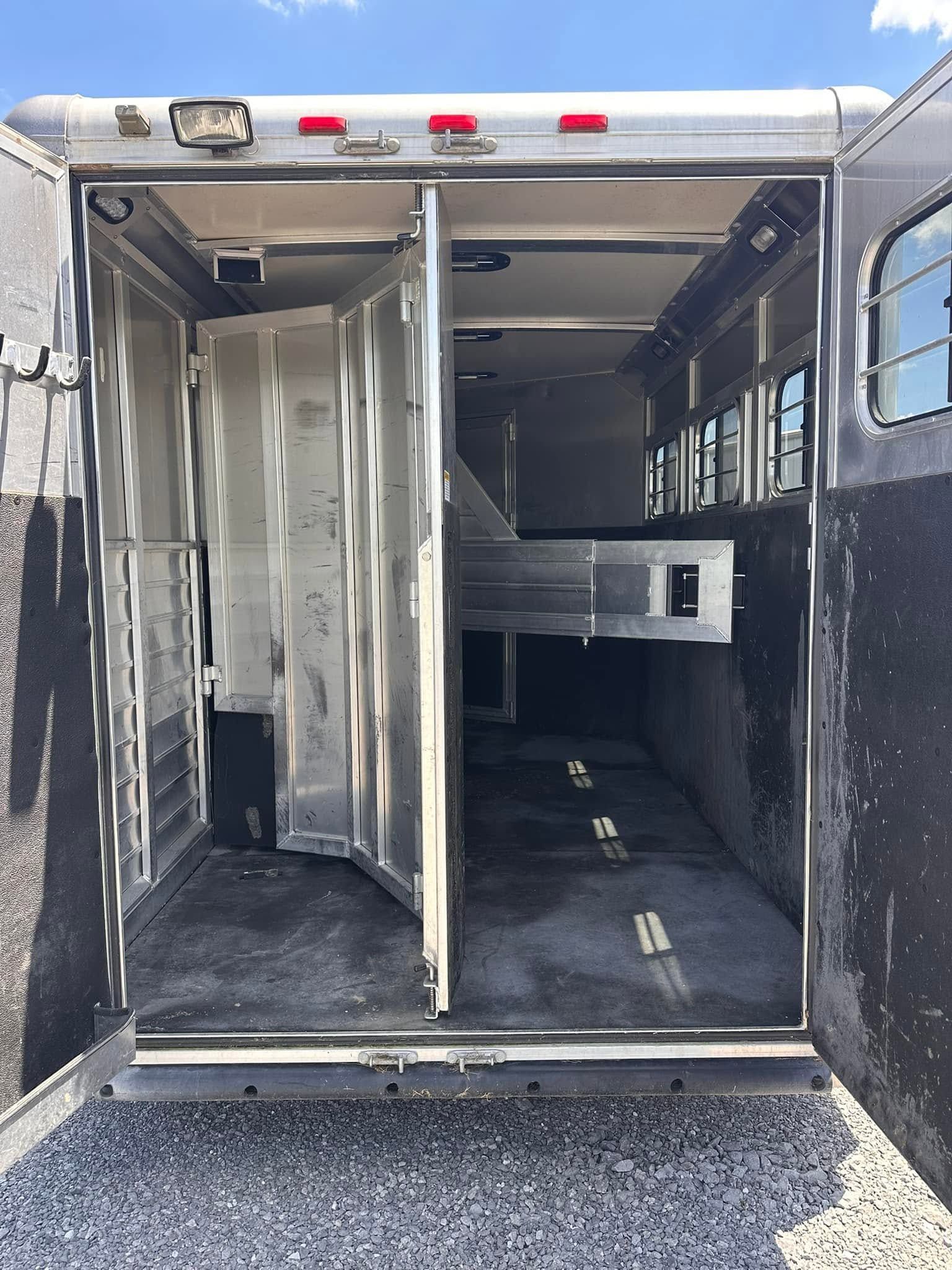 Open trailer with metal partitions and black floor, viewed from the rear on gravel