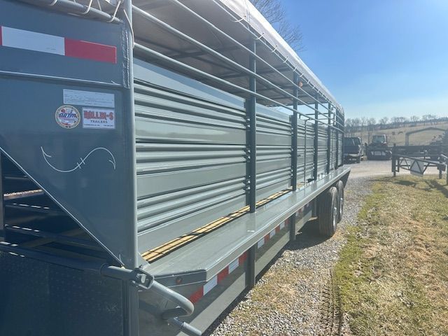 Gray livestock trailer with horizontal slats, parked outdoors on a sunny day.